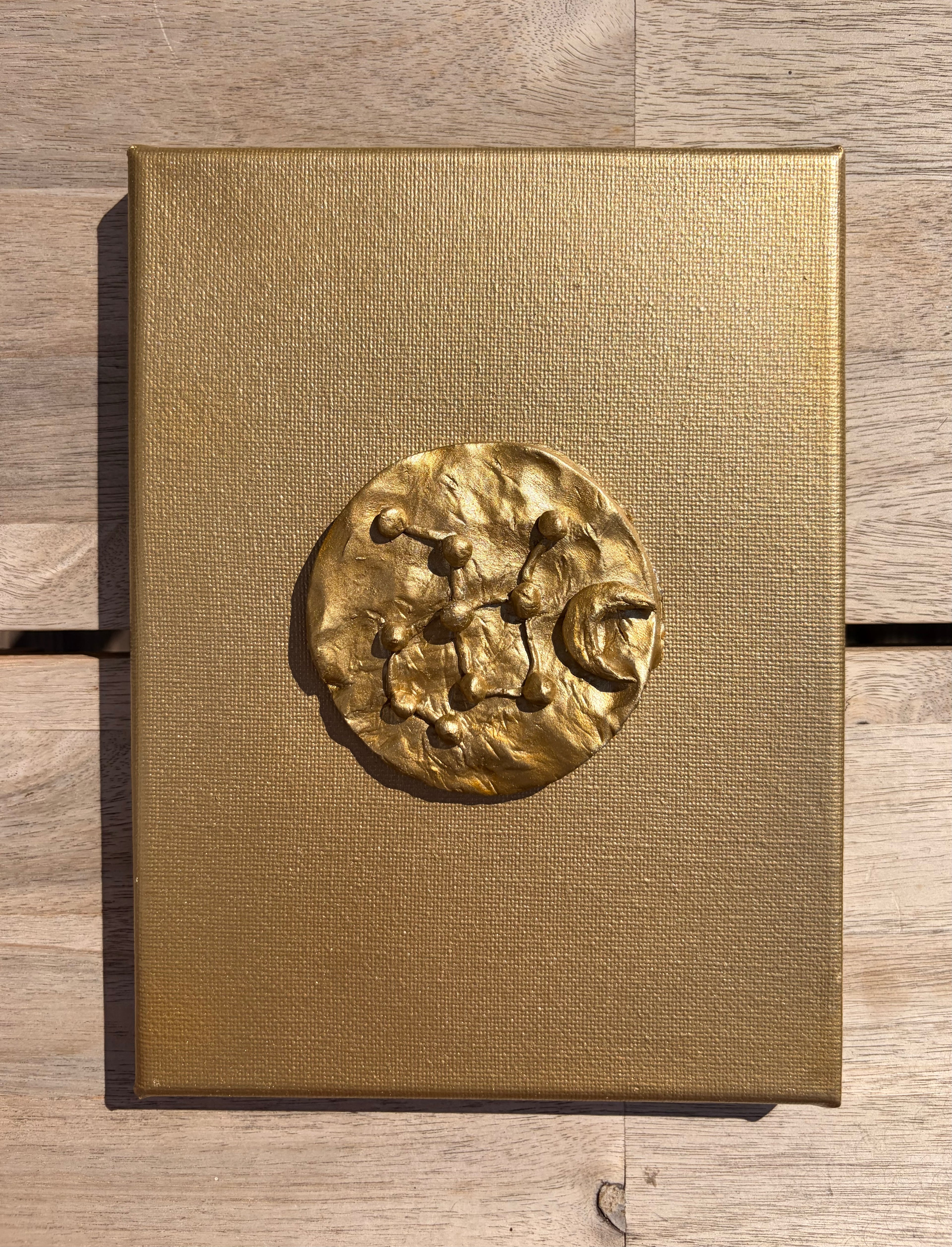 Astra ceramic art on gold canvas, raised metallic gold constellation design against wooden background