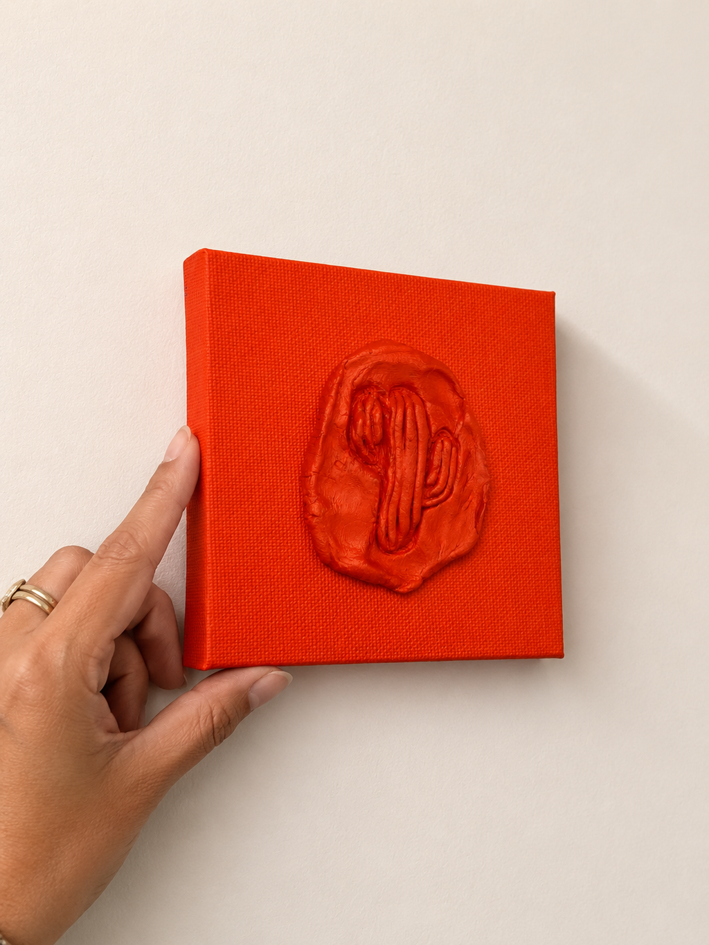 Cactus Arancia — a small orange ceramic cactus emblem mounted on a red box canvas, photographed against a plain white background.