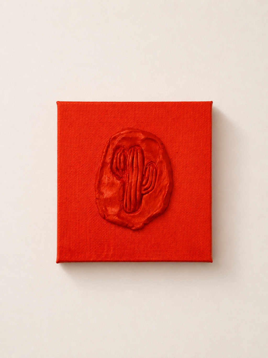 Cactus Arancia — a small orange ceramic cactus emblem mounted on a red box canvas, photographed held against a white background.