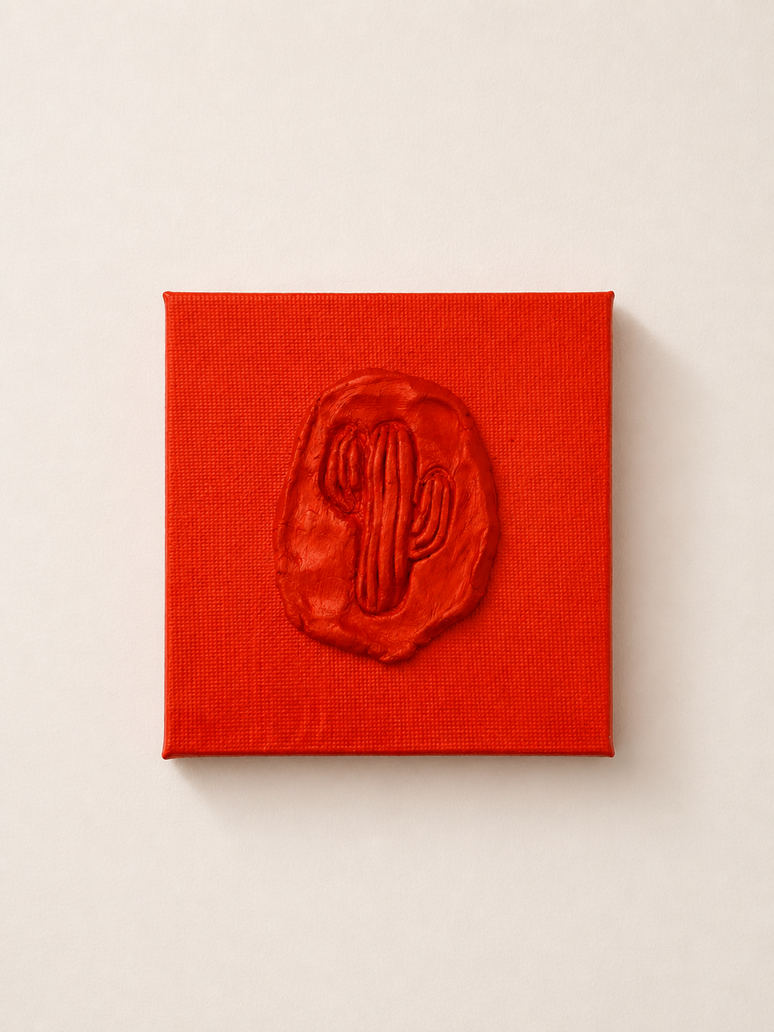Cactus Arancia — a small orange ceramic cactus emblem mounted on a red box canvas, photographed held against a white background.