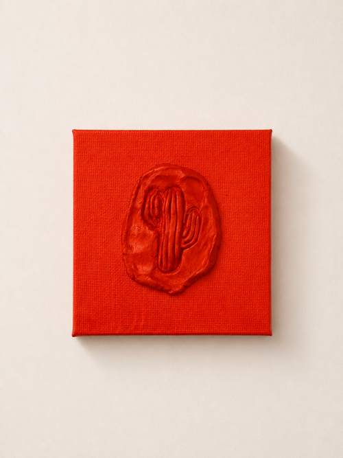 Cactus Arancia — a small orange ceramic cactus emblem mounted on a red box canvas, photographed held against a white background.