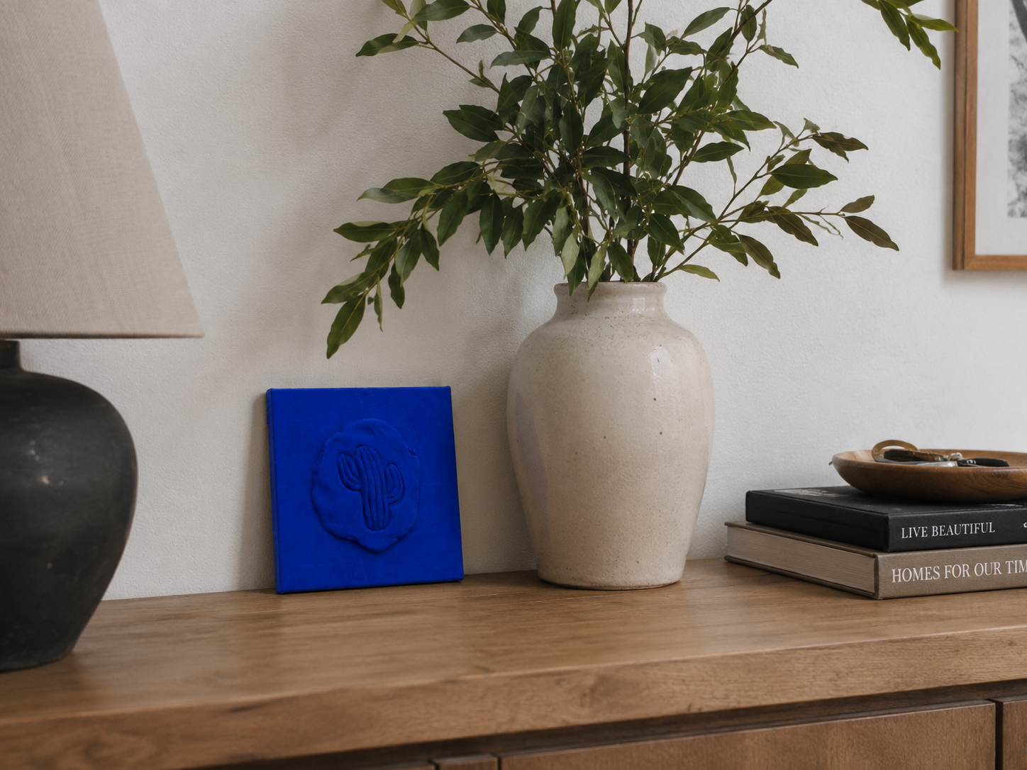 Cactus Blu — a small blue ceramic cactus emblem mounted on a red box canvas, photographed against a console table