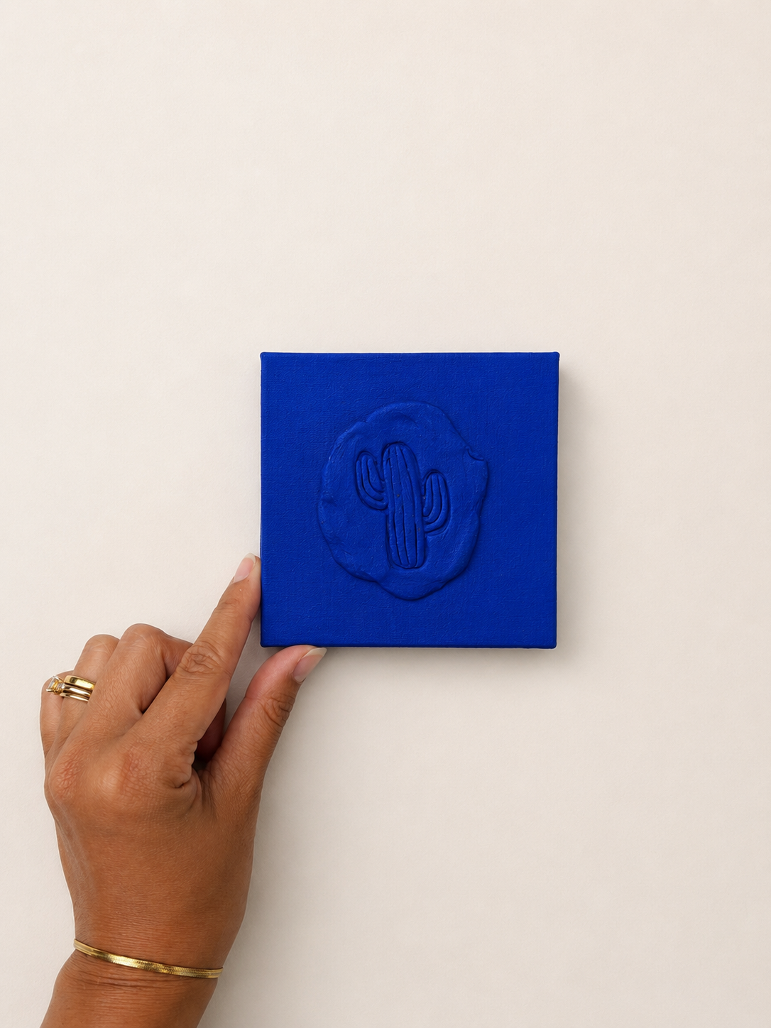Cactus Blu — a small blue ceramic cactus emblem mounted on a red box canvas, photographed against a plain white background.
