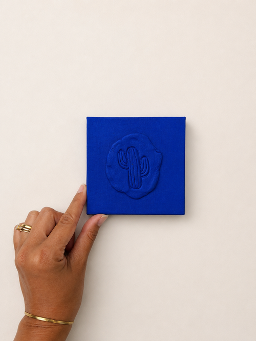 Cactus Blu — a small blue ceramic cactus emblem mounted on a red box canvas, photographed against a plain white background.
