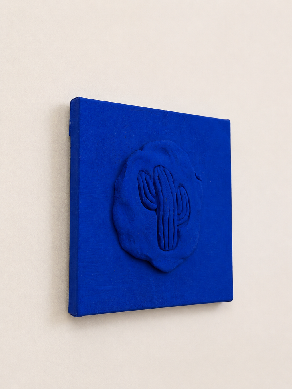 Cactus Blu — a small blue ceramic cactus emblem mounted on a red box canvas, photographed against a plain white background, different angle