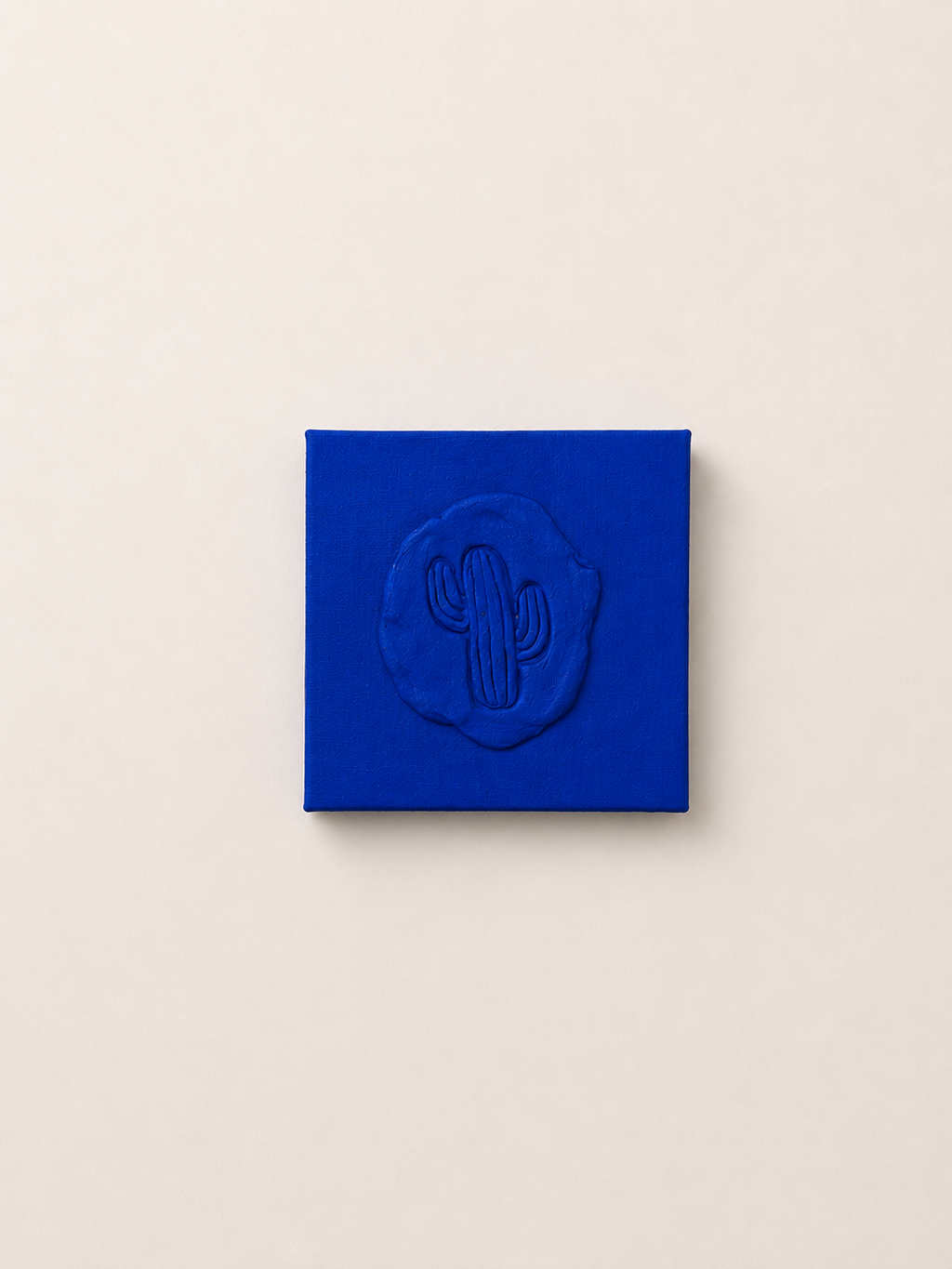 Cactus Blu — a small blue ceramic cactus emblem mounted on a red box canvas, photographed against a plain white background wall 