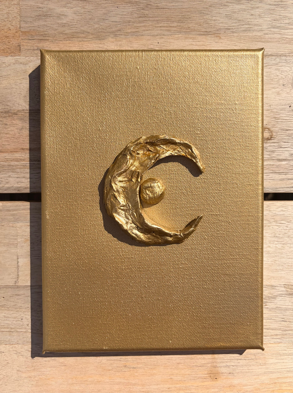 Luna ceramic art on gold canvas, raised metallic gold crescent moon and star design, against wooden top