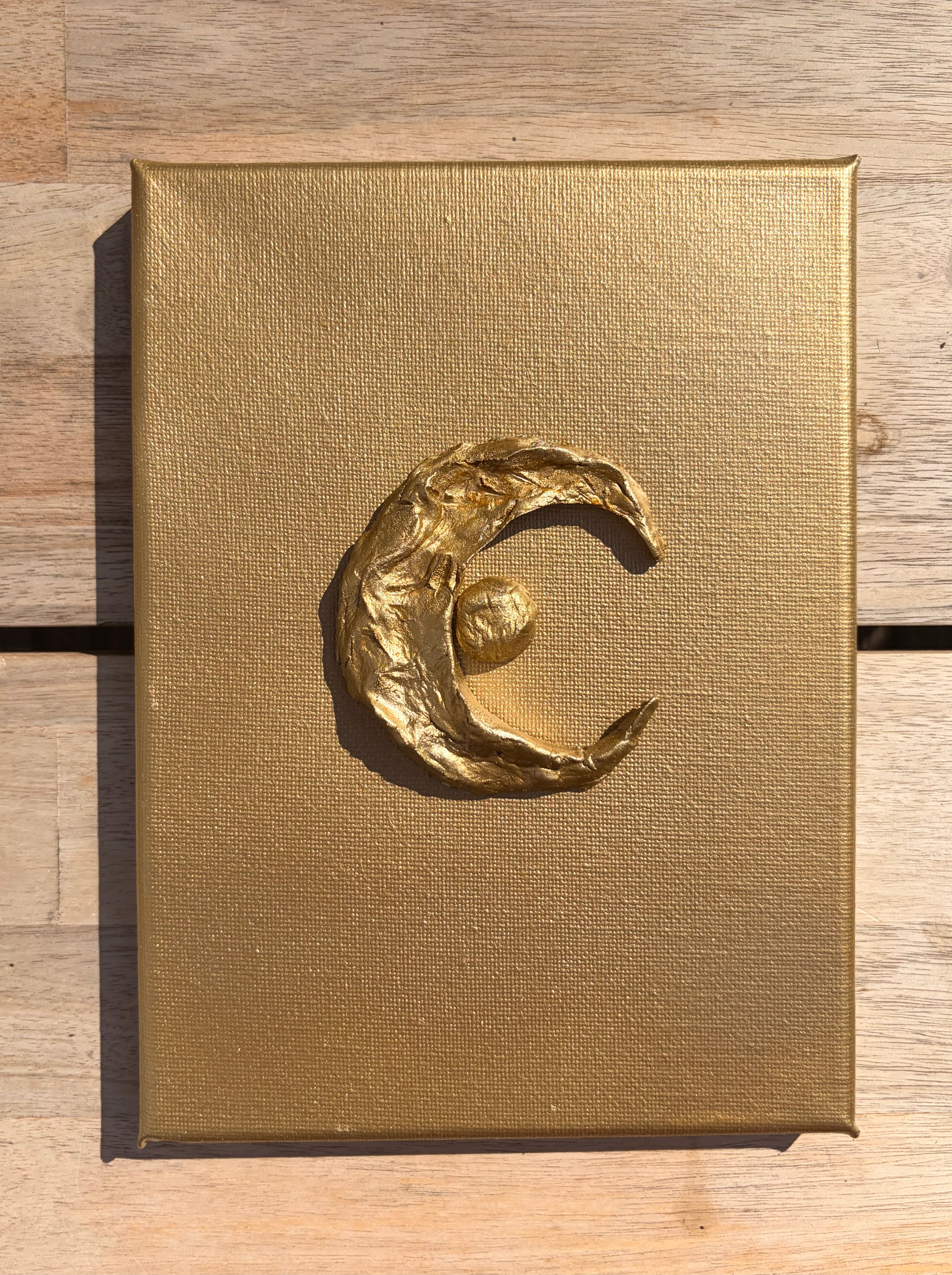 Luna ceramic art on gold canvas, raised metallic gold crescent moon and star design, against wooden top