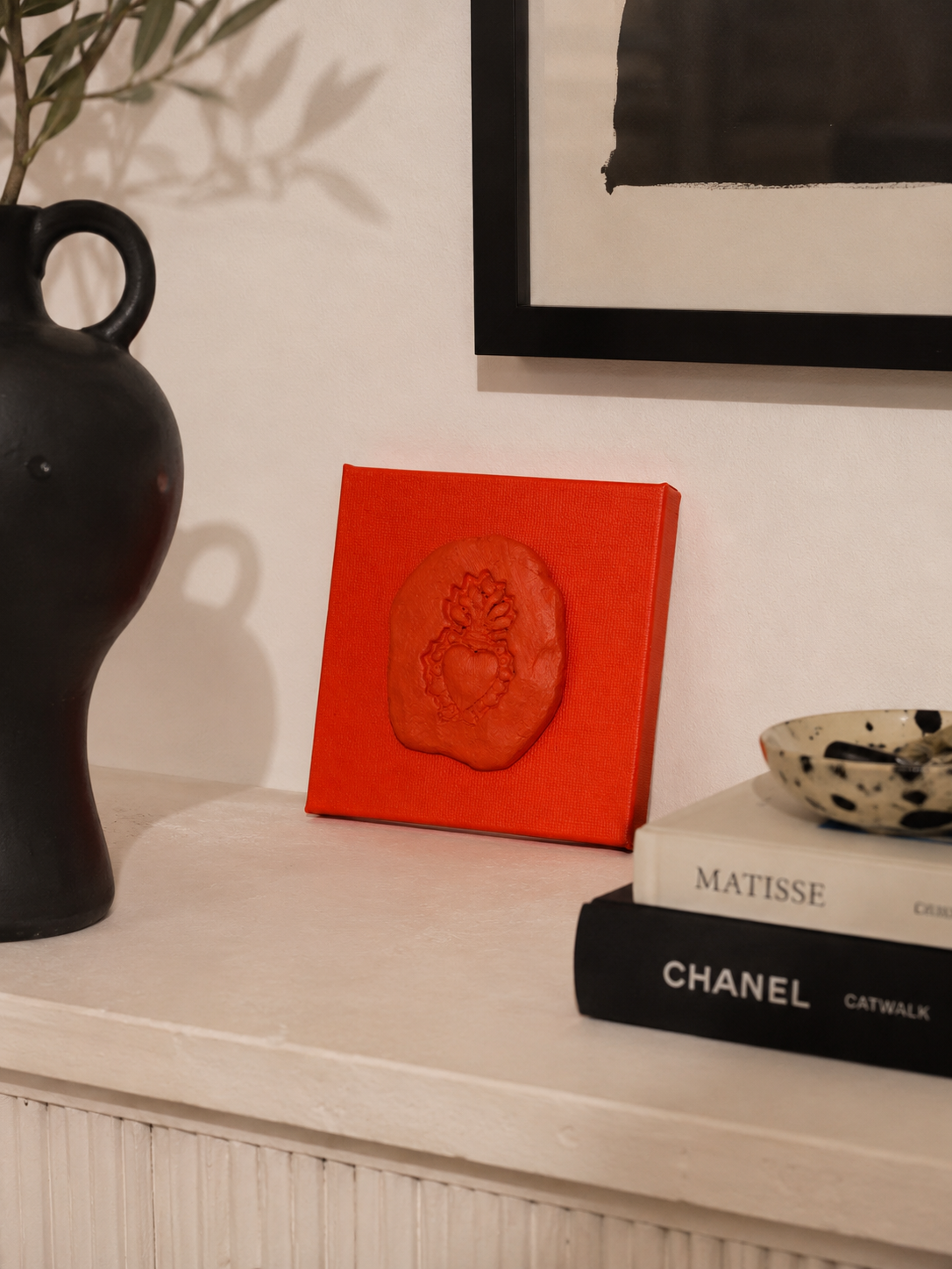 Sacro Cuore Arancia — a small orange ceramic sacred heart emblem mounted on a orange box canvas, photographed against a console table