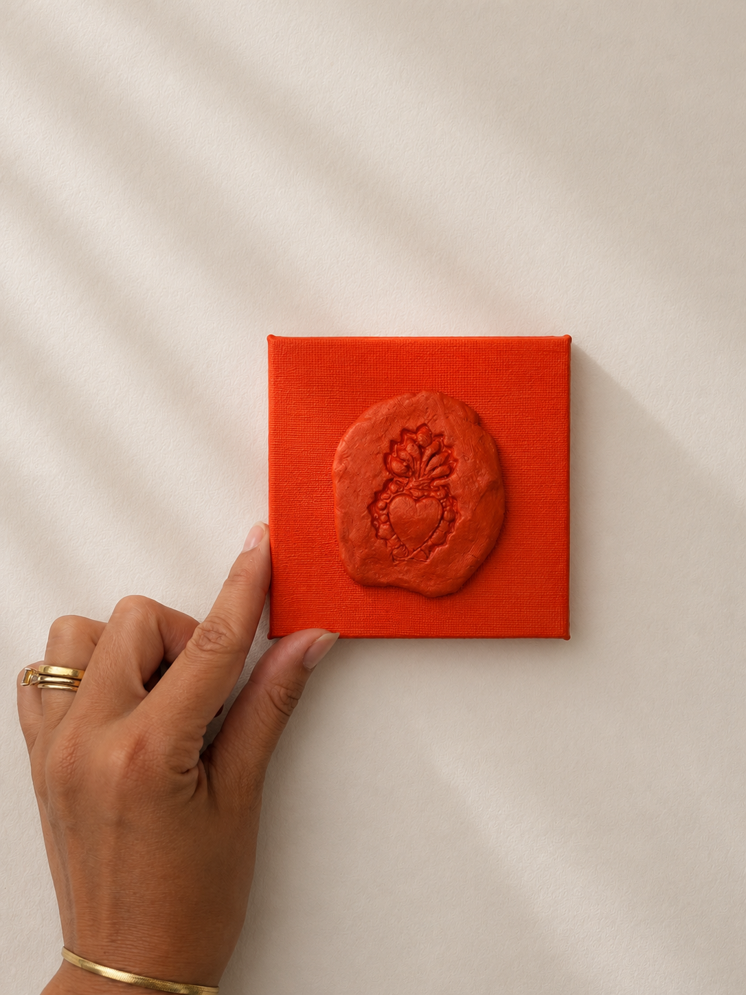 Sacro Cuore Arancia — a small orange ceramic sacred heart emblem mounted on a orange box canvas, photographed against a plain white background.
