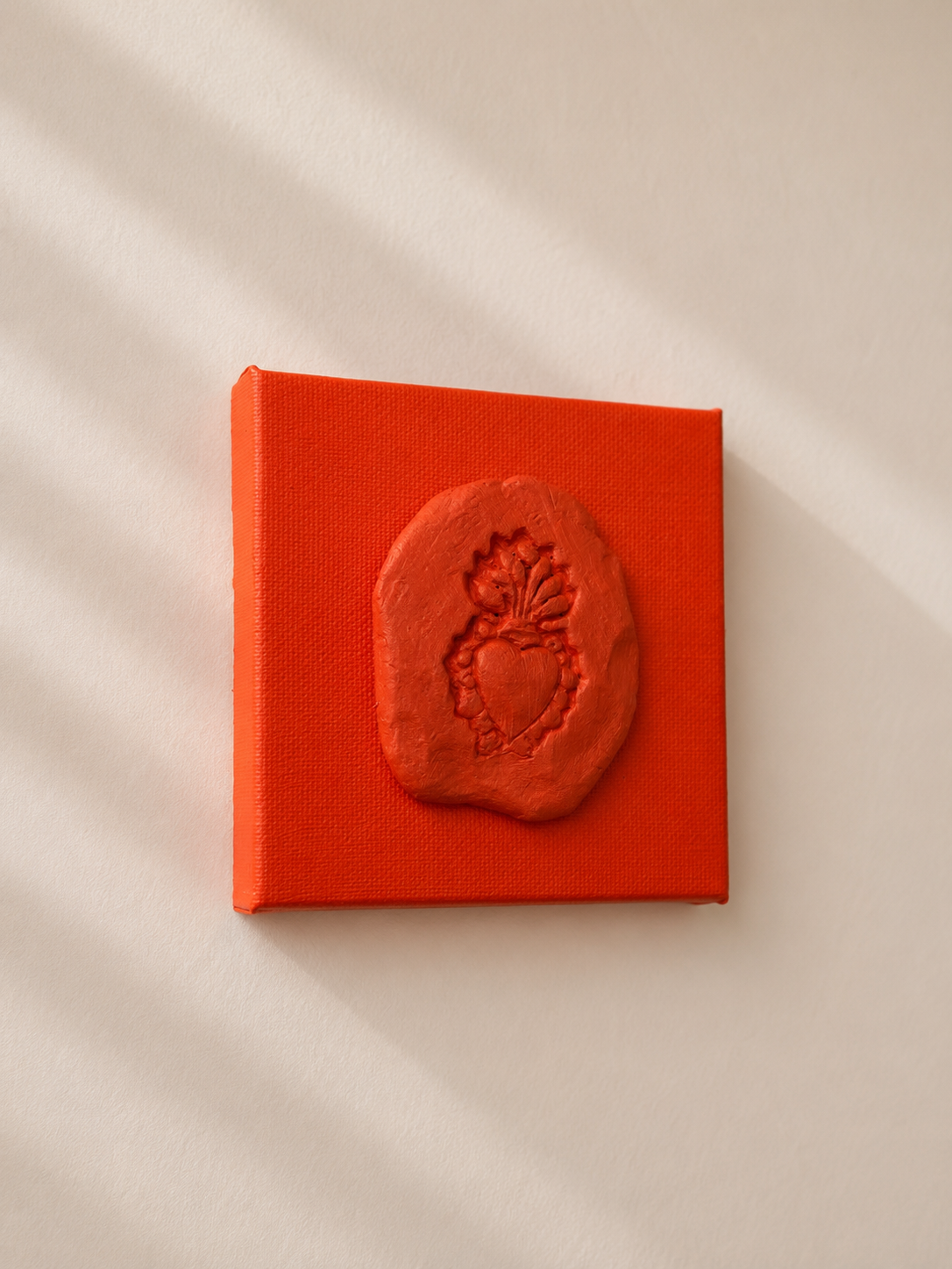 Sacro Cuore Arancia — a small orange ceramic sacred heart emblem mounted on a orange box canvas, photographed against a plain white background, side angle