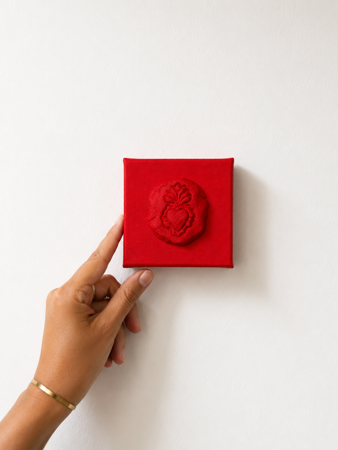 Sacro Cuore Rosso Grande — a small red ceramic sacred heart emblem mounted on a red box canvas, photographed held against a white background