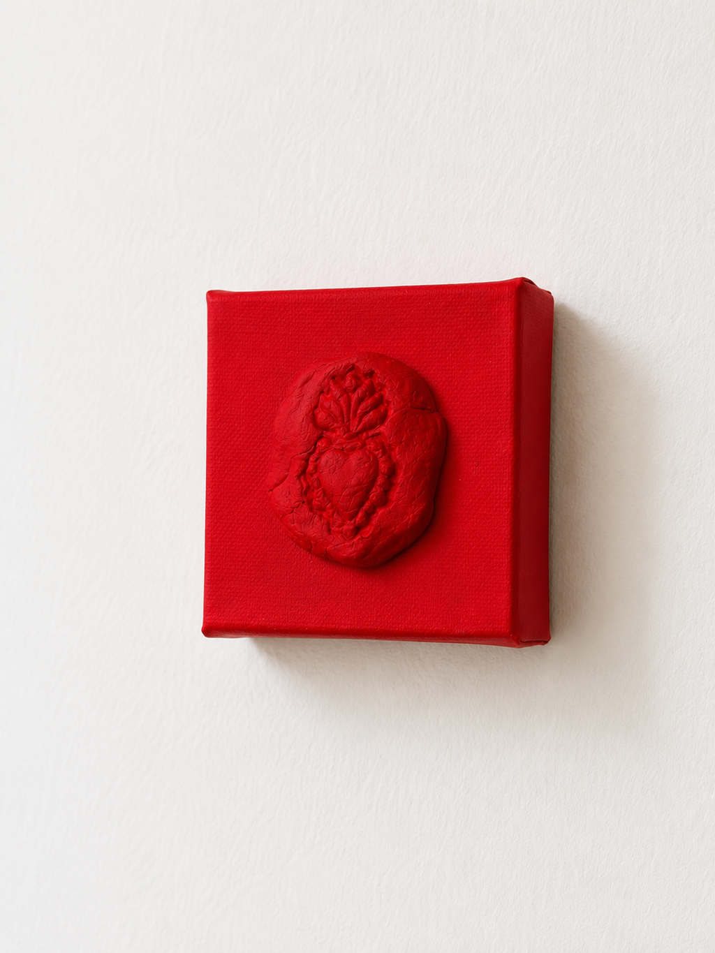 Sacro Cuore Rosso Grande — a small red ceramic sacred heart emblem mounted on a red box canvas, photographed held against a white background at a different angle