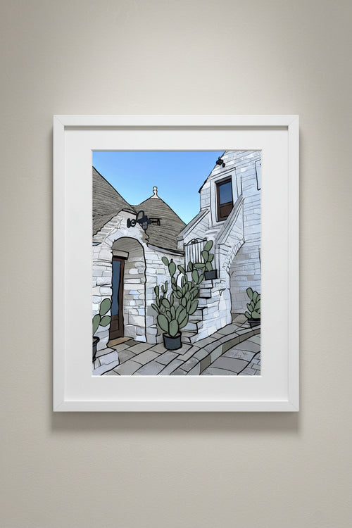 Framed Alberobello print of trulli houses and cacti hung on a wall